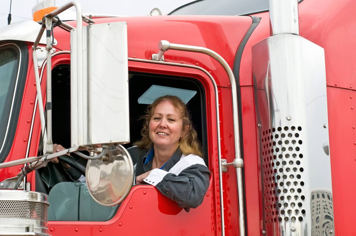 Portrait Of Smiling Young Woman Woman truck driver smiling from the window of a red semi truck