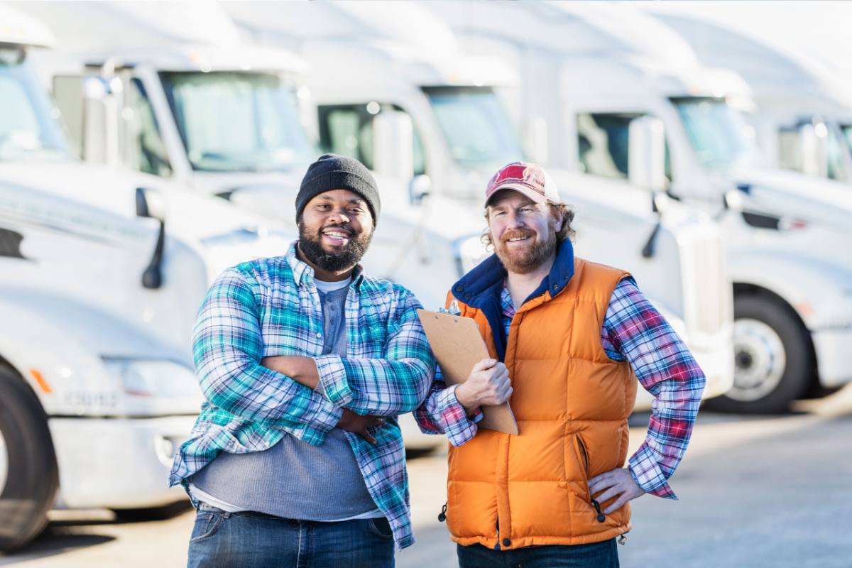 Two-men-in-front-of-fleet-of-trucks-2 Fleet manager and driver in front of a fleet of semi trucks